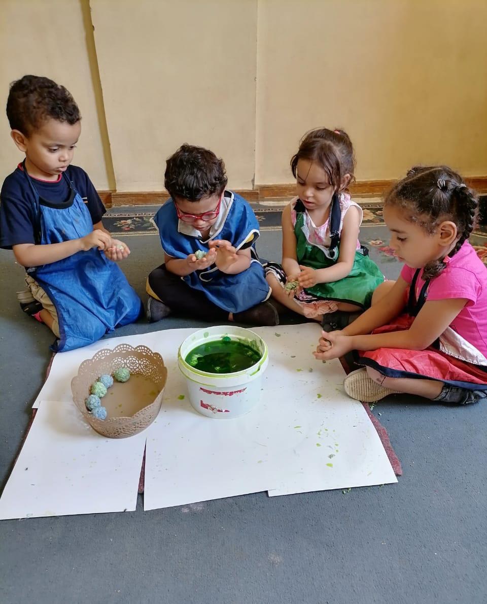 Four young children sitting on the floor, shaping green clay together at Rifka's House.